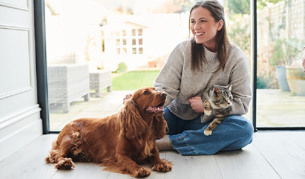Una donna sorride coccolando il suo cane e il suo gatto: per il loro benessere è importante fare attenzione anche alle allergie alimentari nei pet