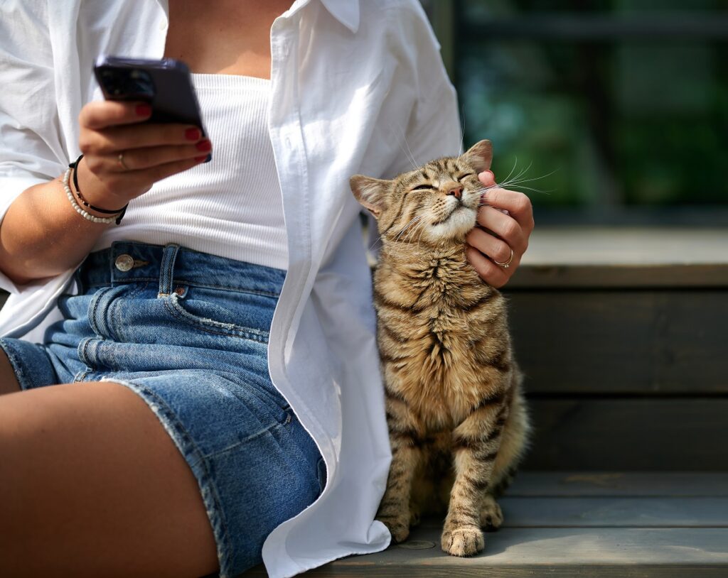 Una donna seduta accanto al suo gatto lo accarezza con una mano