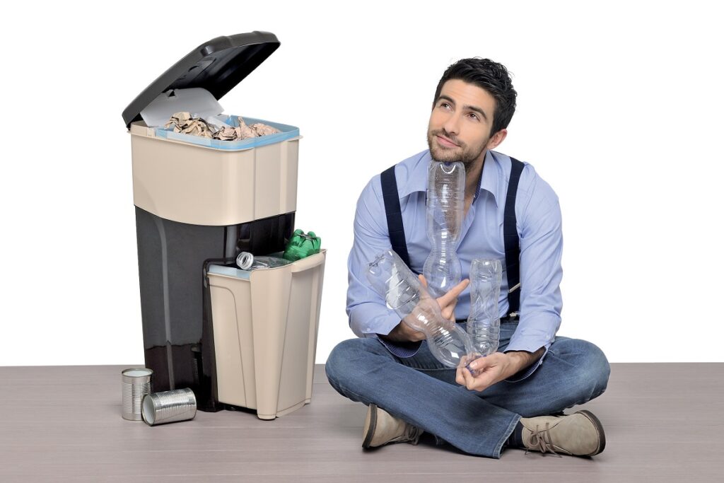 Un uomo seduto per terra pensa a come poter riciclare alcune bottiglie di plastica