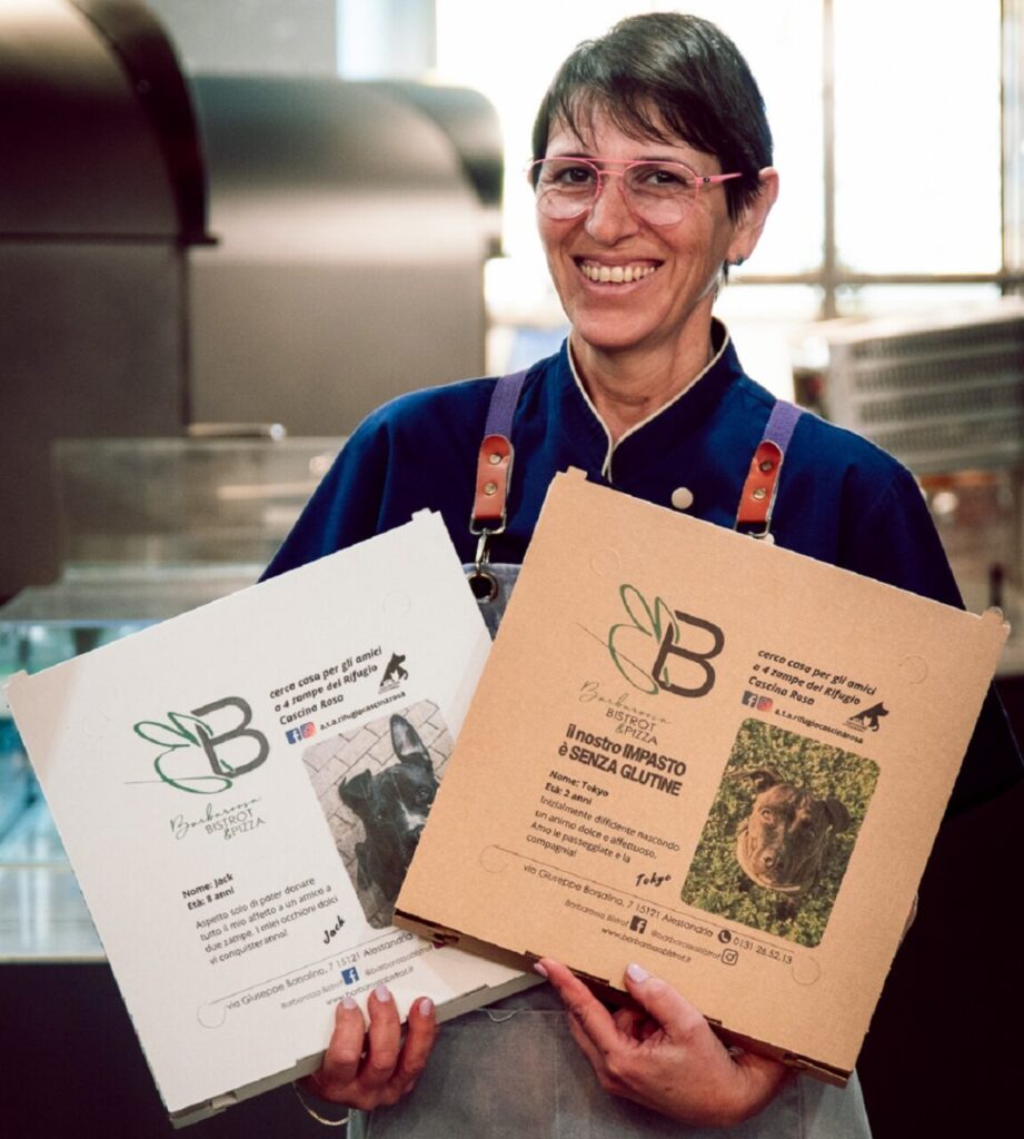 Eliana Amato, ideatrice del progetto Adotta una coda, tiene in mano due cartoni della pizza con le foto e le storie di cani da adottare