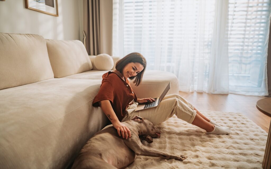 Una donna a casa lavora al computer e si gode la compagnia del suo cane: vivere con cani o gatti aiuta a sertirsi meno soli e non solo