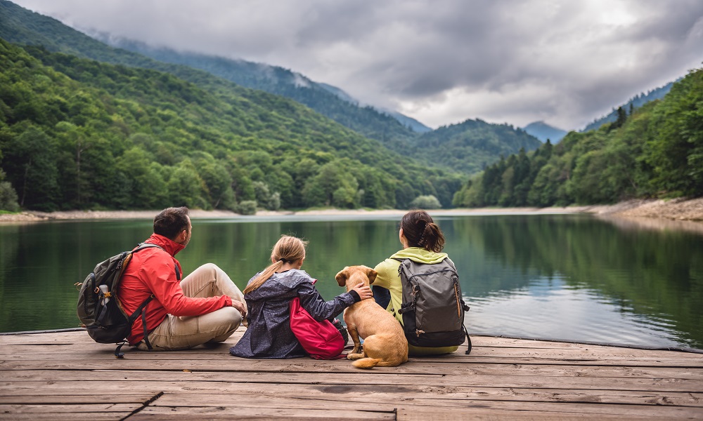 Vacanze pet friendly: una famiglia seduta con il proprio cane sulla riva di un lago